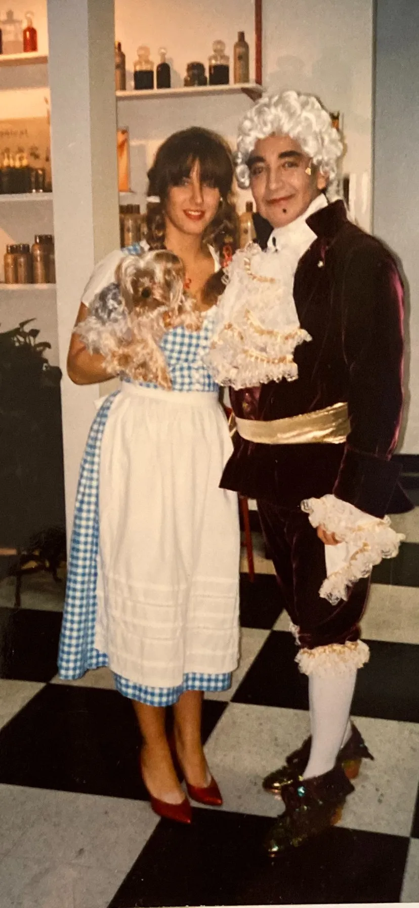 Archival costume party photo of a woman dressed as Dorothy from The Wizard of Oz holding a small dog, beside L.A. Monroe co-founder Luis in an aristocrat costume