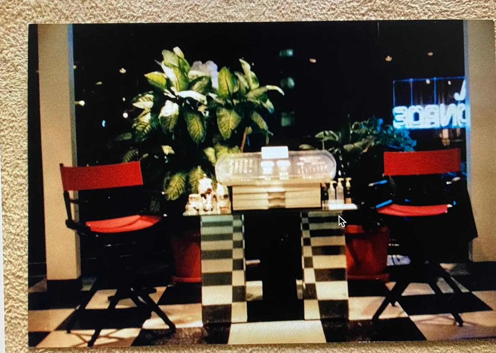 Archival photograph of the L.A. Monroe makeup area - two red director's chairs across a checkered floor with a large tropical plant and the 'MONROE' neon visible behind