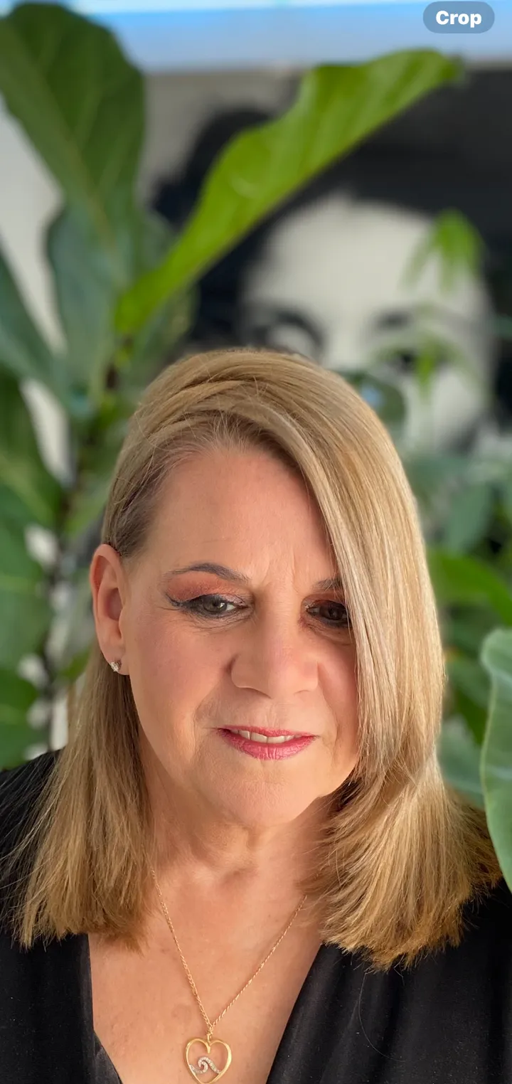 Mid-length honey-blonde hair with soft layers and side part, mature client portrait among tropical plants