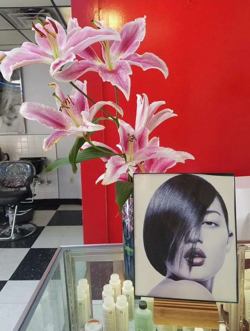 Pink stargazer lilies beside a framed black-and-white portrait of a sleek bob hairstyle against a red wall