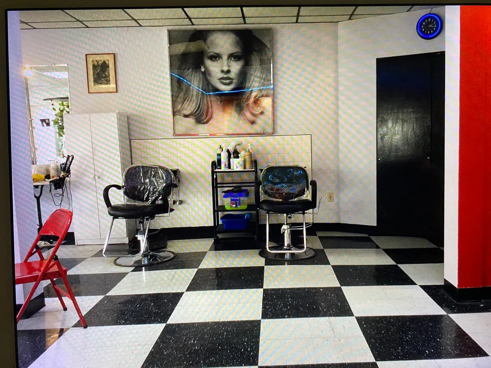 Salon interior with two styling chairs, a black-and-white checkered floor, and a large portrait artwork on the wall
