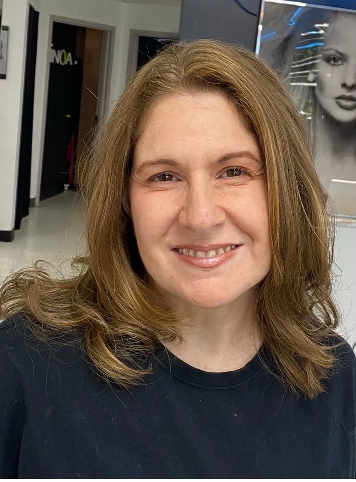 Mid-length brown hair with warm caramel highlights and soft layers, client smiling portrait