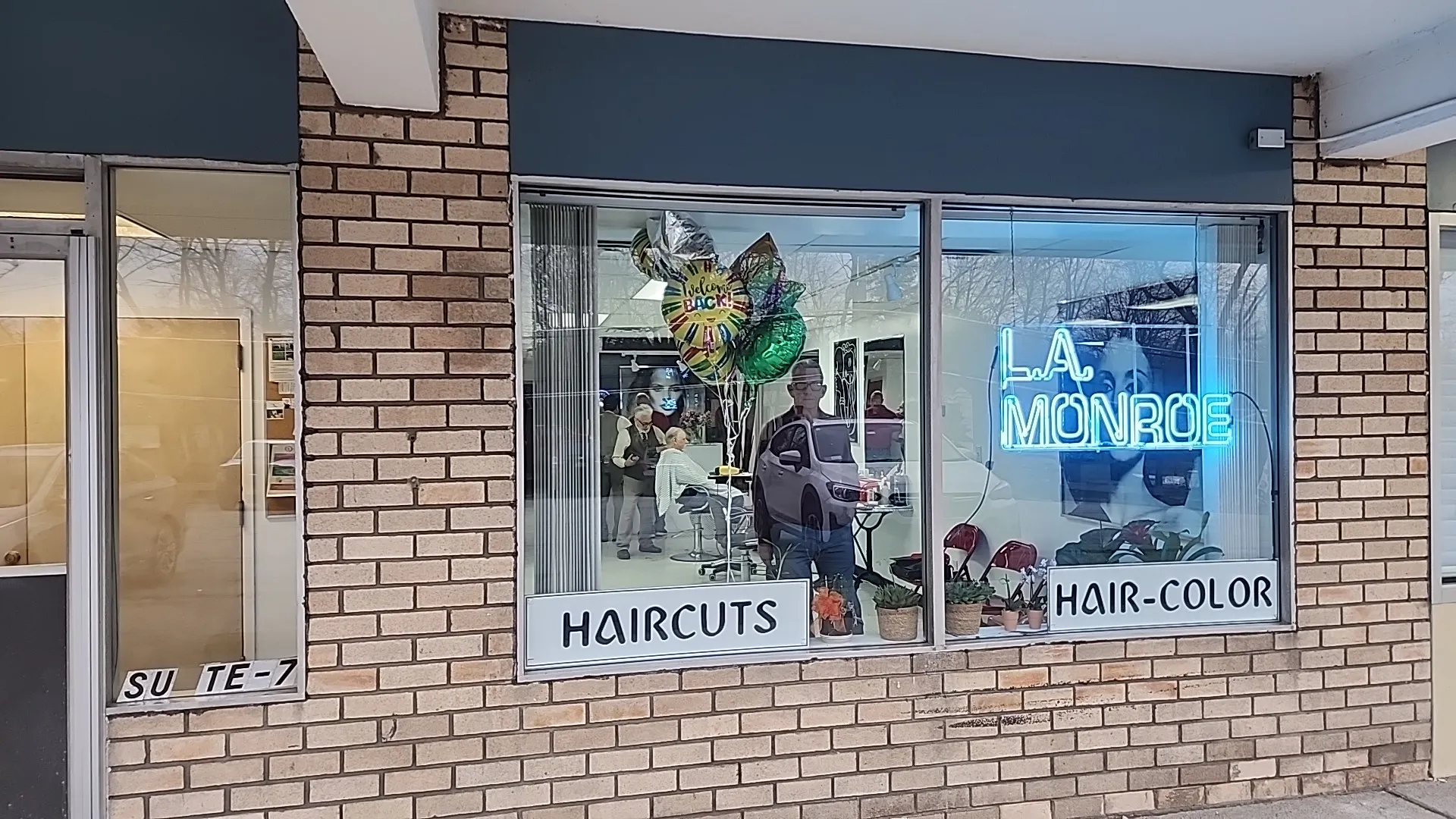 Storefront window of LA Monroe Hair Studio with neon sign and HAIRCUTS / HAIR-COLOR decals